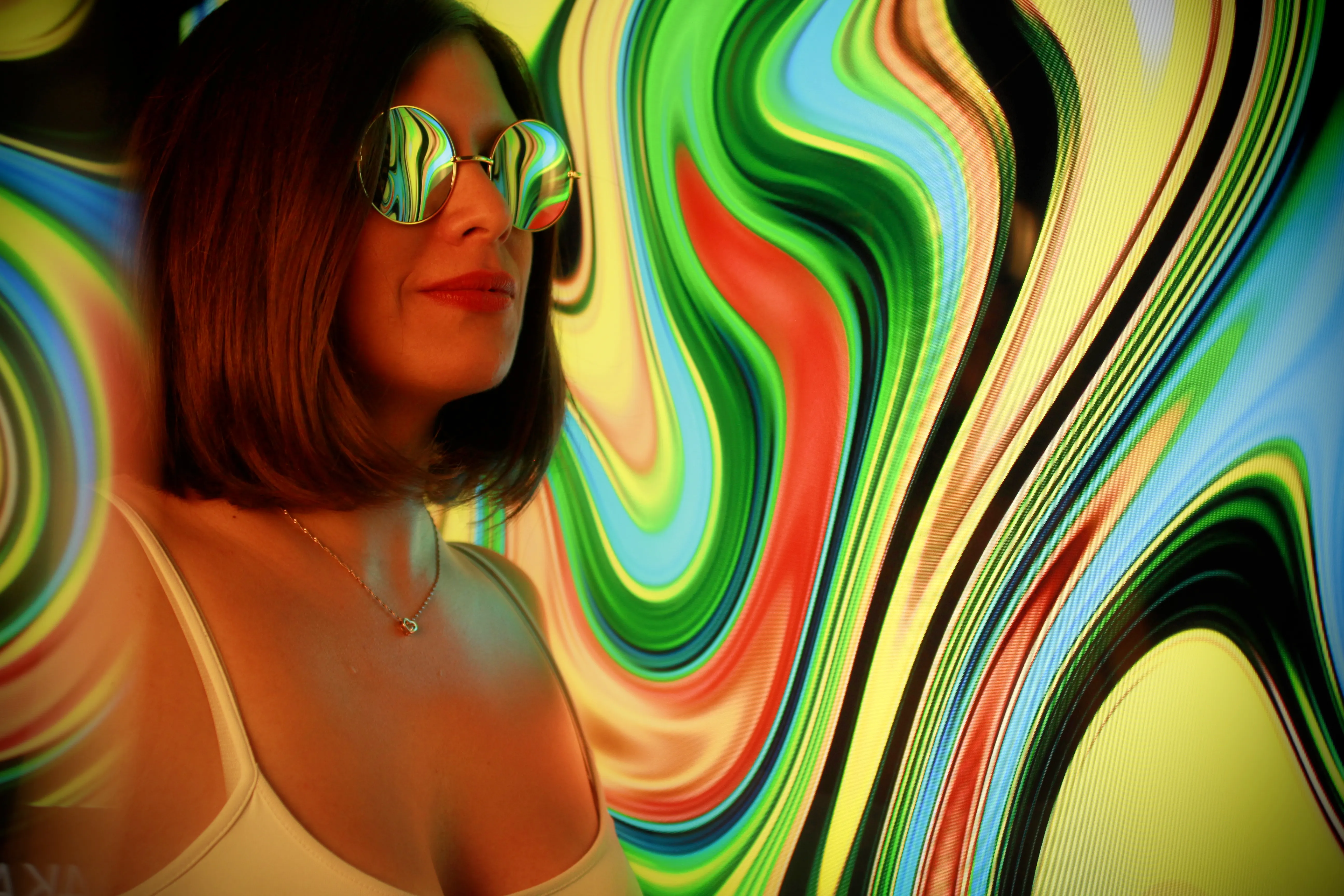 Frau mit rotem Lippenstift und runder verspiegelter Sonnenbrille vor bunten Farbwirbeln
