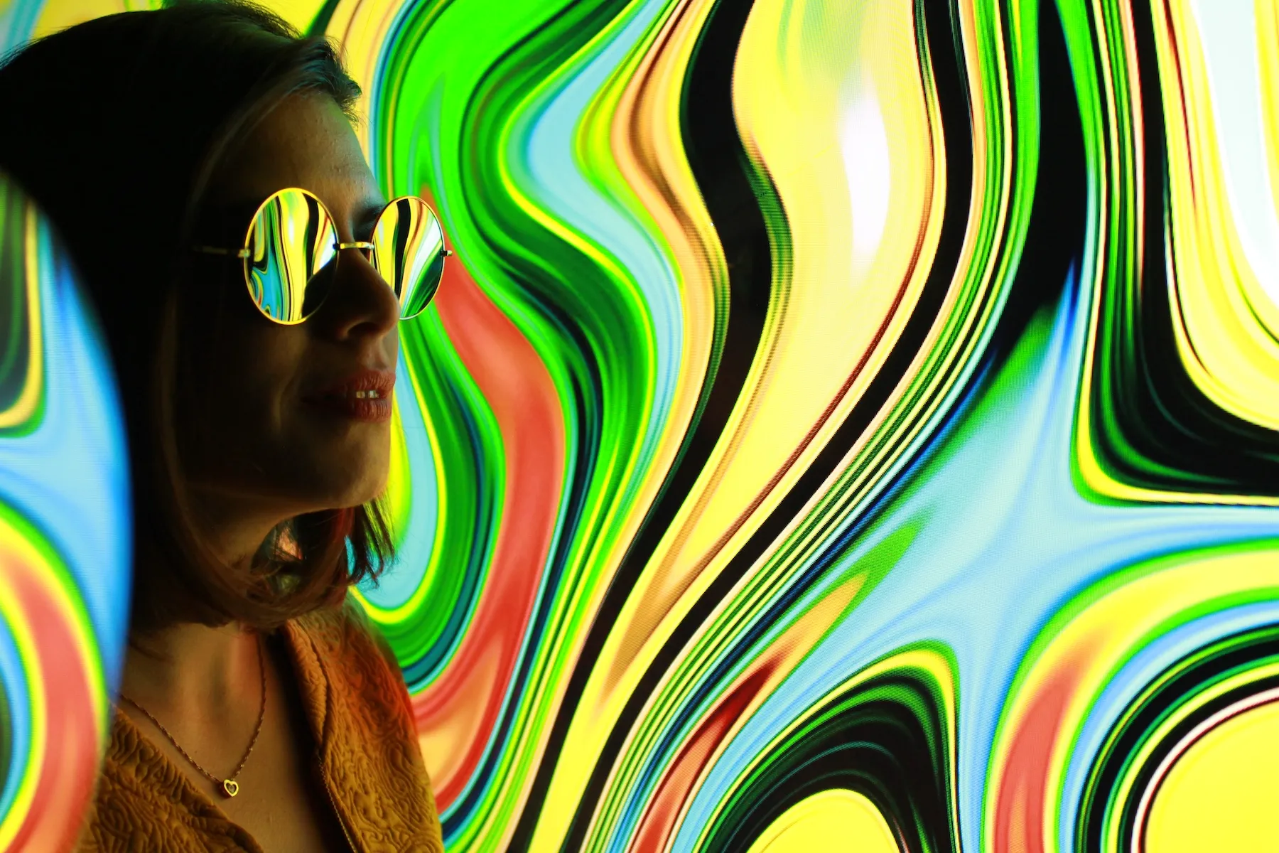 Frau mit verspiegelter runder Sonnenbrille vor psychedelischen Farbwirbeln